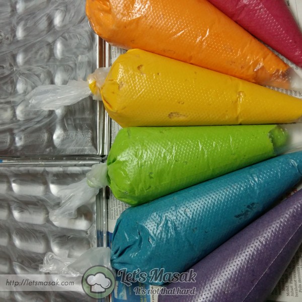 Masukkan ke dalam piping bag untuk setiap warna berlainan. Potong hujung muncung piping bag tersebut dan paipkan atas loyang lidah kucing.